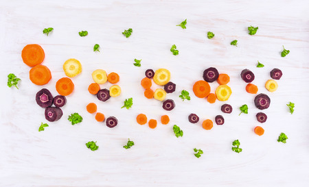 Word veggy of colorful chopped carrots with parsley leaves on white wooden background, top viewの写真素材
