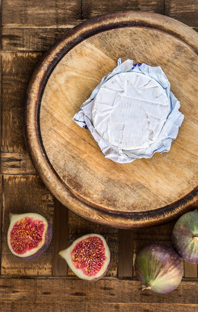 Cheese in paper on old wooden circular cutting board with slices of figs, top viewの写真素材