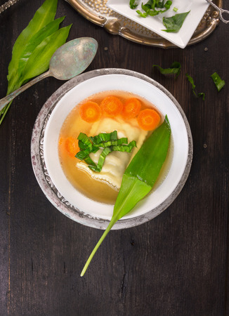 soup with ravioli,carrots and ramson leafs in silver plate with vintage spoon on dark wooden tableの写真素材