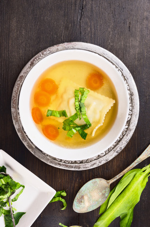 Clear soup with ravioli , carrots and ramson on  dark  old wooden background, top viewの写真素材