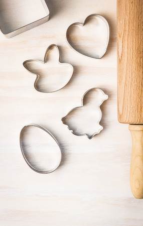 Easter biscuit cutter: rabbit, chicken, egg, heart and dough roll on white wooden backgroundの写真素材