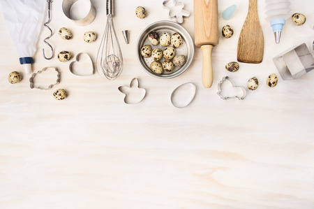 Easter bake tools with quail eggs and biscuit cutter on white wooden background, top view, place for...