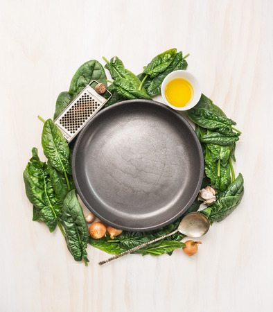 Fresh spinach leaves with cooking ingredients: oil, nutmeg, garlic and olnion around a gray empty plate on white wooden background, top view, place for textの写真素材