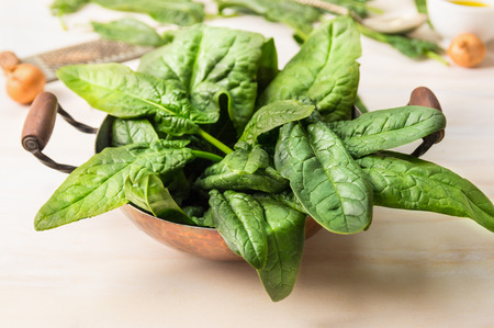 Raw spinach in copper pan on white wooden background, close up