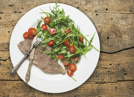 beef with rocket salad and tomatoes on old wood table, dietetic foodの写真素材