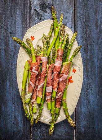 Green asparagus wrapped in ham in plate on rustic blue wooden backgroundの写真素材