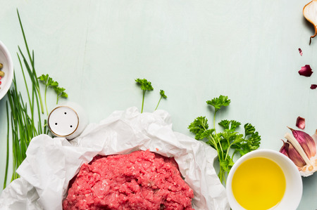 Raw minced meat with fresh ingredients and oil top view frame