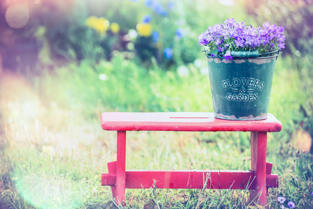 Vintage bucket with garden flowers on red little stool over summer nature backgroundの写真素材