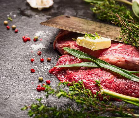 Raw beef steak. Preparation with old meat cleaver, butter and fresh herbsの写真素材