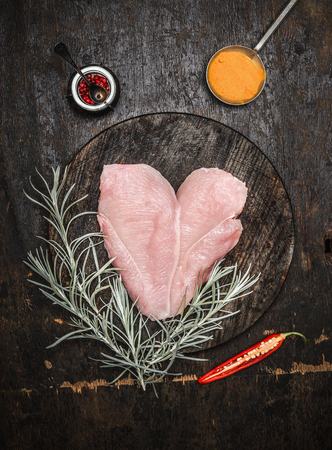 Raw chicken breast in heart shape with herbs and spices on dark wooden background, top view. Diet and health food conceptの写真素材