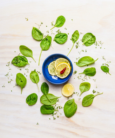 Fresh delicious baby spinach around bowl with lemon and spices on white wooden background, top view. Clean food concept.の写真素材