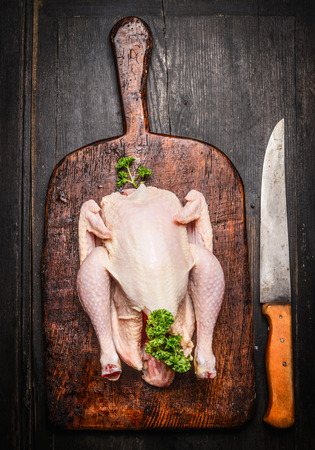 Raw whole chicken on vintage cutting board with kitchen knife on rustic wooden background, top viewの写真素材