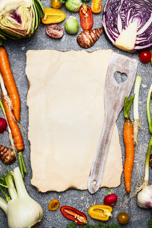 Healthy food and tasty vegetarian cooking background with colorful assortment of farm vegetables around blank sheet of paper with wooden spoon, top view, frame.の写真素材