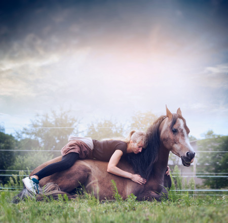 Woman lies and embraces a resting horse on nature background with skyの写真素材