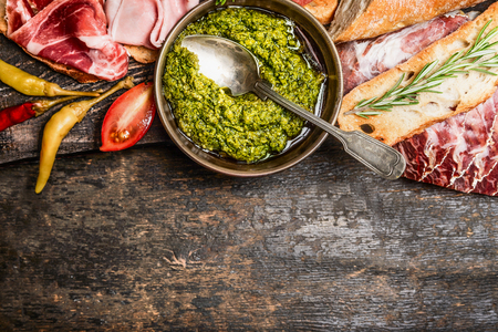 Green pesto and meat plate with bread and antipasti on rustic wooden background, top view, border. Italian food conceptの写真素材