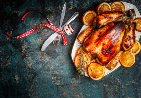 Roasted turkey or chicken with orange slices in plate for Christmas dinner served with fork,knife and festive decoration on dark rustic background, top viewの写真素材