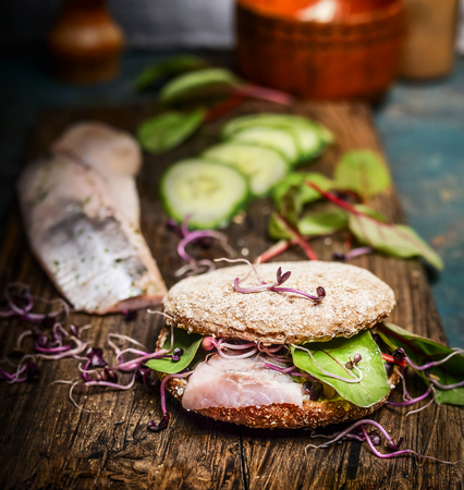 Healthy fish sandwich with herring, cucumber and sprouts on rustic kitchen table, side viewの写真素材
