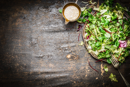 Fresh mixed green salad with oil dressing rustic wooden background, top view. Healthy food or vegetarian eating concept.の写真素材