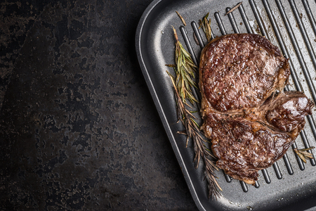 Grilled ribeye steak on grill iron pan on  grunge metal background, close up.  Top view, place for text.の写真素材