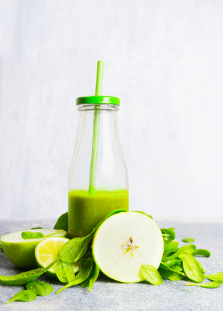 Green smoothie bottle with straw and green ingredients on light wooden background, side view. Healthy lifestyle and detox or diet  food conceptの写真素材