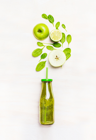 Green smoothie drink in bottle with straw  and  ingredients ( spinach,apple, lime )  on white wooden background, top viewの写真素材