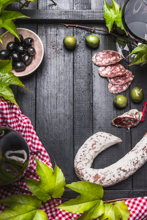 Italian food lifestyle background with salami, wine,olives and grape leaves on dark wooden background, top view, frame.の写真素材