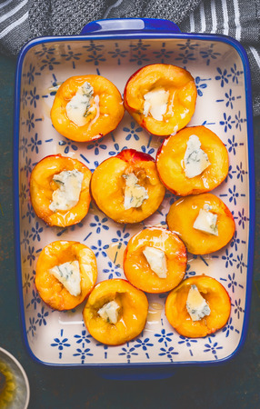 Halves of peaches in baking dish with cheese and honey, top view, close up. Summer fruits cookingの写真素材