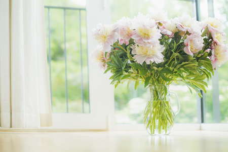 Big beautiful pale pink peonies bouquet in glass vase over window background. Light Home  decoration with flowers and vase. Living room interiorの写真素材