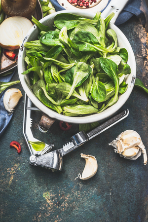 Green fresh organic lettuce leaves in old enameled colander on dark rustic kitchen table with tools and ingredients for salad making, top viewの写真素材