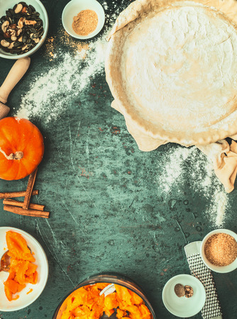 Pumpkin pie cooking : dough in backing form, filling and ingredients on dark rustic background, top view , retro styledの写真素材