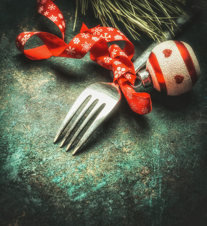 Festive Christmas table place setting with fork, ribbon ,ball and pine on dark rustic vintage background, top view, close upの写真素材