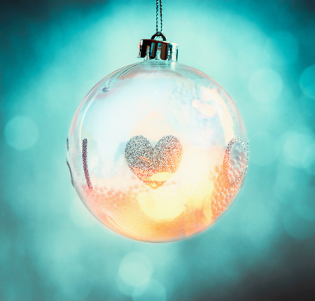 Hanging glass Christmas ball with heart and bokeh lighting on  turquoise blue backgroundの写真素材