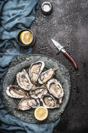 Open raw oysters on vintage plate with lemon and oysters knife, dark rustic background with water drops , top viewの写真素材