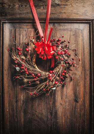 Handmade Christmas wreath hanging on wooden door with red ribbon and berries , front viewの写真素材