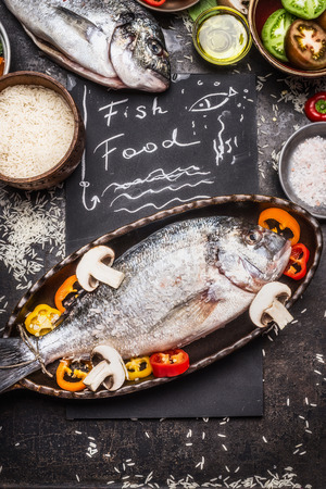 Fish food text with raw dorado, rice and vegetables cooking ingredients on dark rustic background, top view. Healthy food or diet food concept.の写真素材