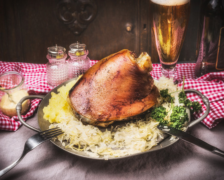 Roasted pork knuckle knuckle with mashed potatoes and braised cabbage boiled in plate with cutlery and beer on rustic table, front view. Country styleの写真素材