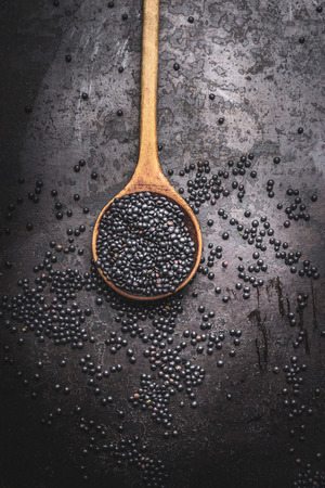 Black beluga lentil seeds in wooden cooking spoon on dark rustic background, top viewの写真素材