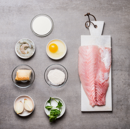 Various cooking ingredients for Fish patties in bowls: fish fillets , egg, shrimps , onion ,bread, flour on on gray stone background  , top viewの写真素材