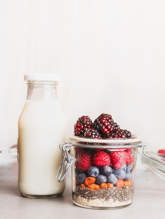 Glass jar with oatmeal , Chia seeds, Goji berries, fresh berries and bottle of milk on white wooden background, front view. Healthy breakfast conceptの写真素材