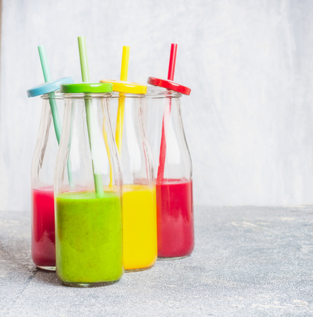 Colorful smoothies assortment in bottles with drinking straws: green, yellow, red, front viewの写真素材
