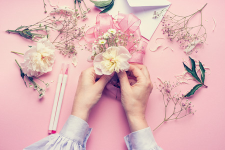 Female hands making lovely floral arrangement with flowers and ribbon on pale pink background, top view. Creative greeting, Invitation and holiday conceptの写真素材