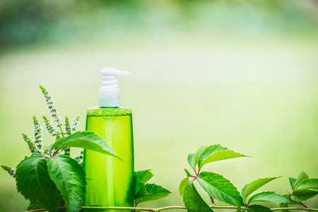 Green cosmetic product bottle for skin, body or hair care with green leaves at green nature background, front view. Natural cosmetic concept, copy spaceの写真素材