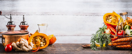 Autumn seasonal  cooking concept. Various autumn seasonal organic vegetables: pumpkin,carrot,paprika,tomatoes,ginger in basket on wooden kitchen desk tables with pot at wall background, front view.の写真素材