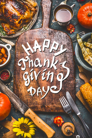 Thanksgiving dinner background with  turkey ,sauce,grilled vegetables,corn ,cutlery ,  pumpkin, fall leaves and text Happy Thanksgiving Day on wooden gutting board, top view.の写真素材