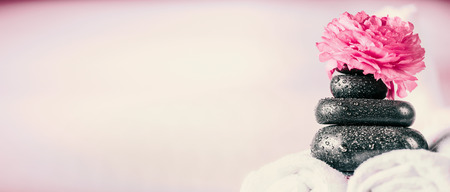Stack of spa massage stones with pink flowers and  towels, wellness background, front view, bannerの写真素材