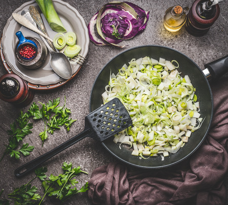 Leeks dishes cooking preparation. Steamed leeks in  frying pan  on rustic kitchen table background, top view. Healthy vegetarian food and eating, clean or diet nutrition conceptの写真素材