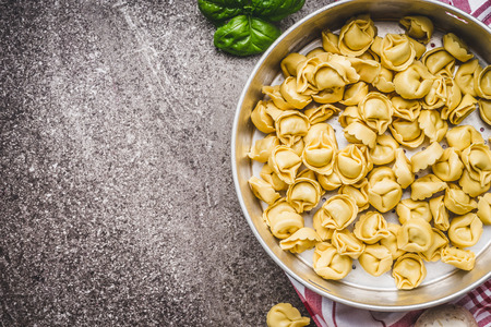 Raw tortellini pasta in bowl, ready for cooking on rustic background , top view. Italian cuisine food conceptの写真素材