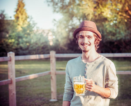 Happy guy in german has a mug of beer on hand and a smile on his face at country nature backgroundの写真素材