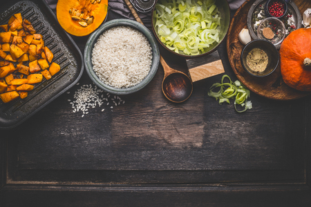 Pumpkin risotto cooking ingredients on dark rustic kitchen table with bowls, spoon and pan, top view, border. Vegetarian food, Clean seasonal eatingの写真素材