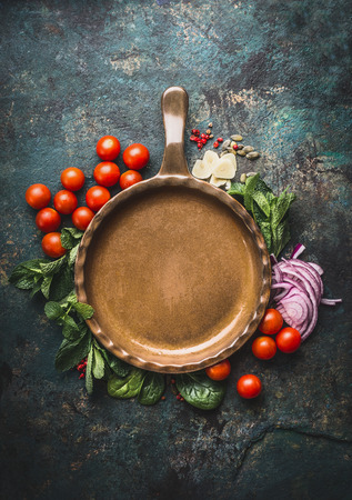 Vegetarian cooking ingredients around frying pan on dark rustic background, place for text, frame. Healthy eating and cooking, clean or diet food conceptの写真素材
